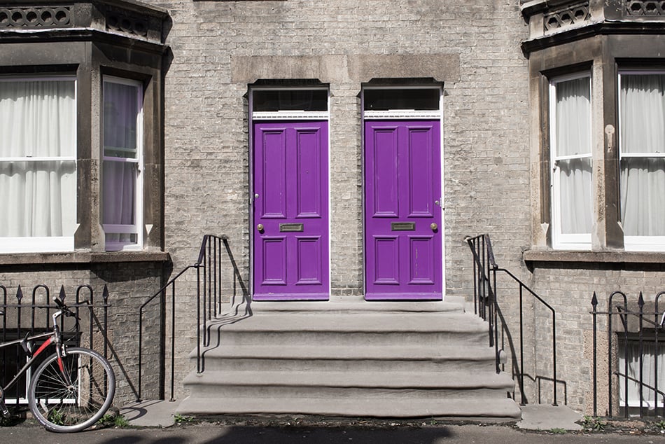 Two Identical Purple Wooden Doors on Grey Exterior